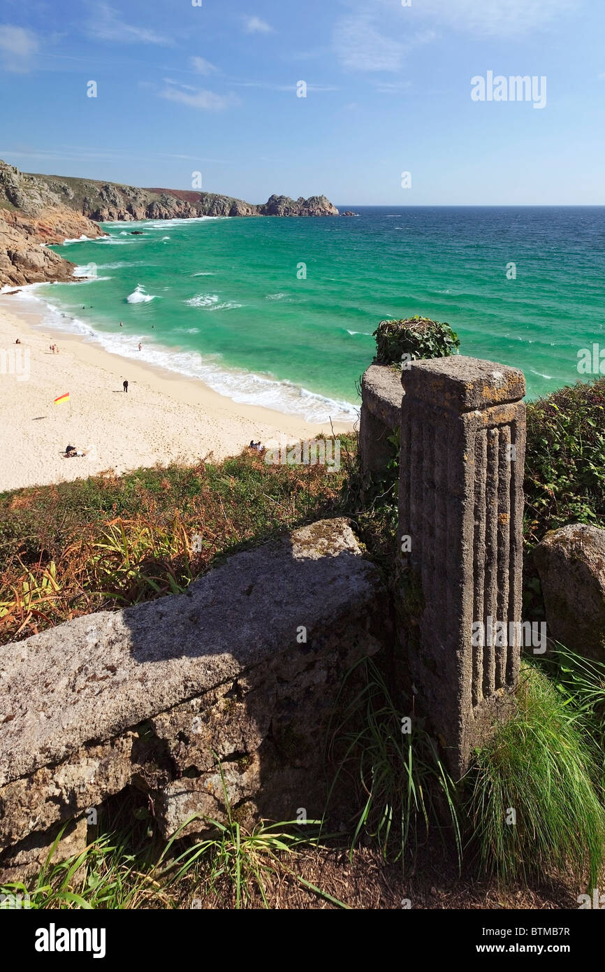 Eine Mauer und Pfeiler bieten Vordergrund Interesse in dieser Ansicht über Porthcurno Strand in Richtung Treen Strand und Logan Rock, Cornwall Stockfoto