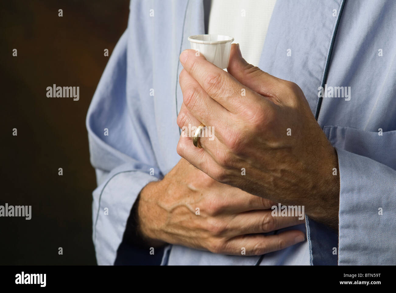 Mann im Bademantel mit Medikamenten in Pappbecher Stockfoto