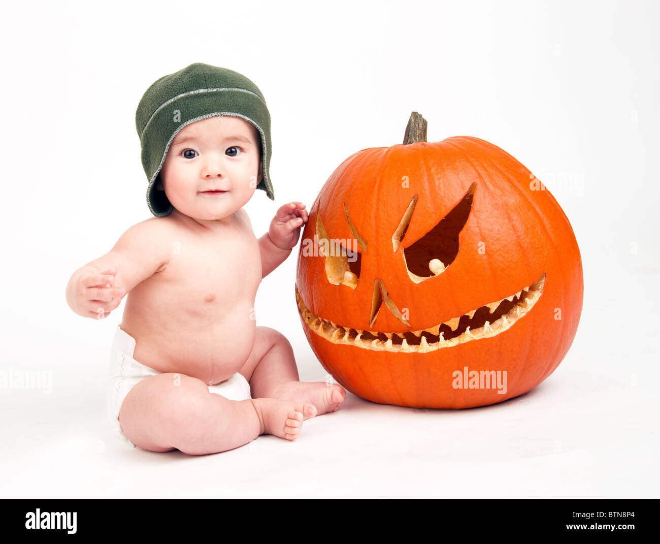 6 Monate altes Baby sitzt von einem geschnitzten Kürbis Stockfoto