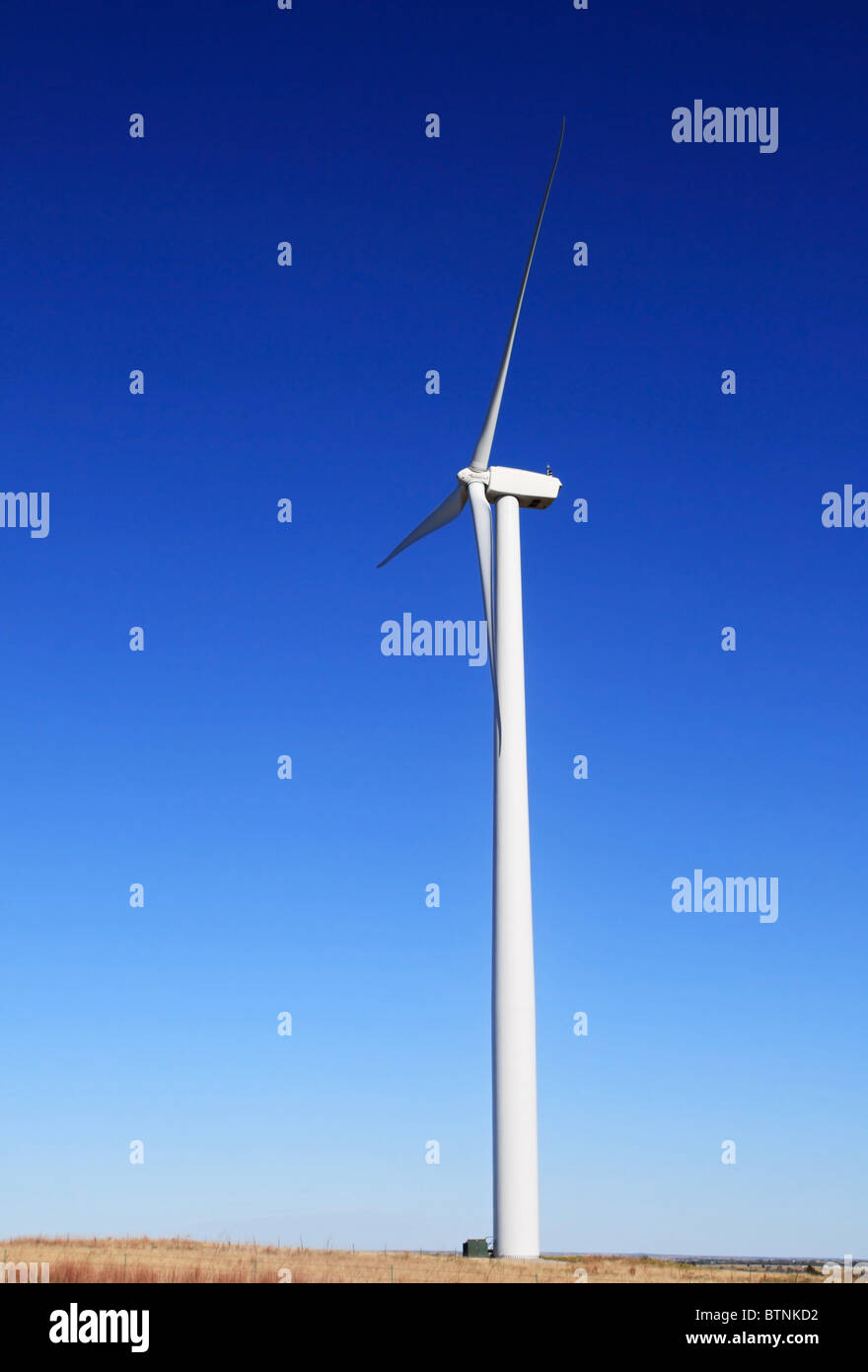 vertikales Bild der hohen weiße elektrische Windmühle oder Wind Turbine auf einem flachen Prärie mit blauem Himmelshintergrund Stockfoto
