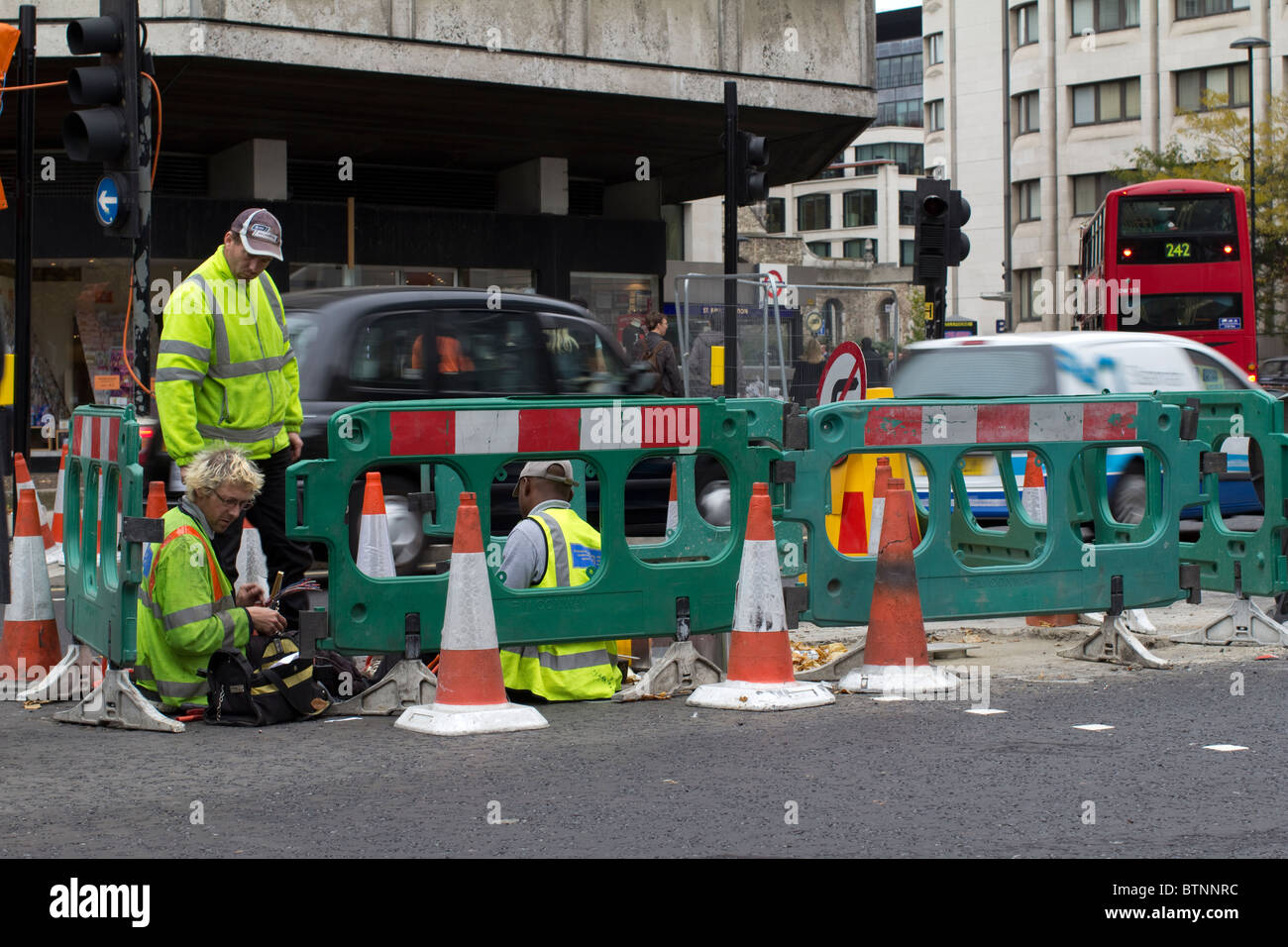 Straßenarbeiten mit Barrieren und Kegeln, Telekommunikationsingenieure arbeiten mitten in Straßenbefestigungskabeln, mit Verkehr in Central London Großbritannien Stockfoto