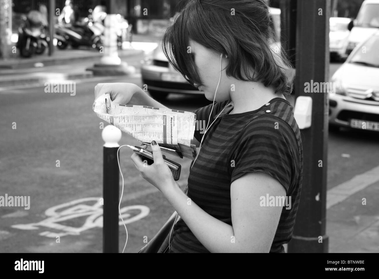 Junge Frau betrachten Cityplan beim Anhören von MP3-Player warten darauf, überqueren Sie die Straße in Paris Stockfoto