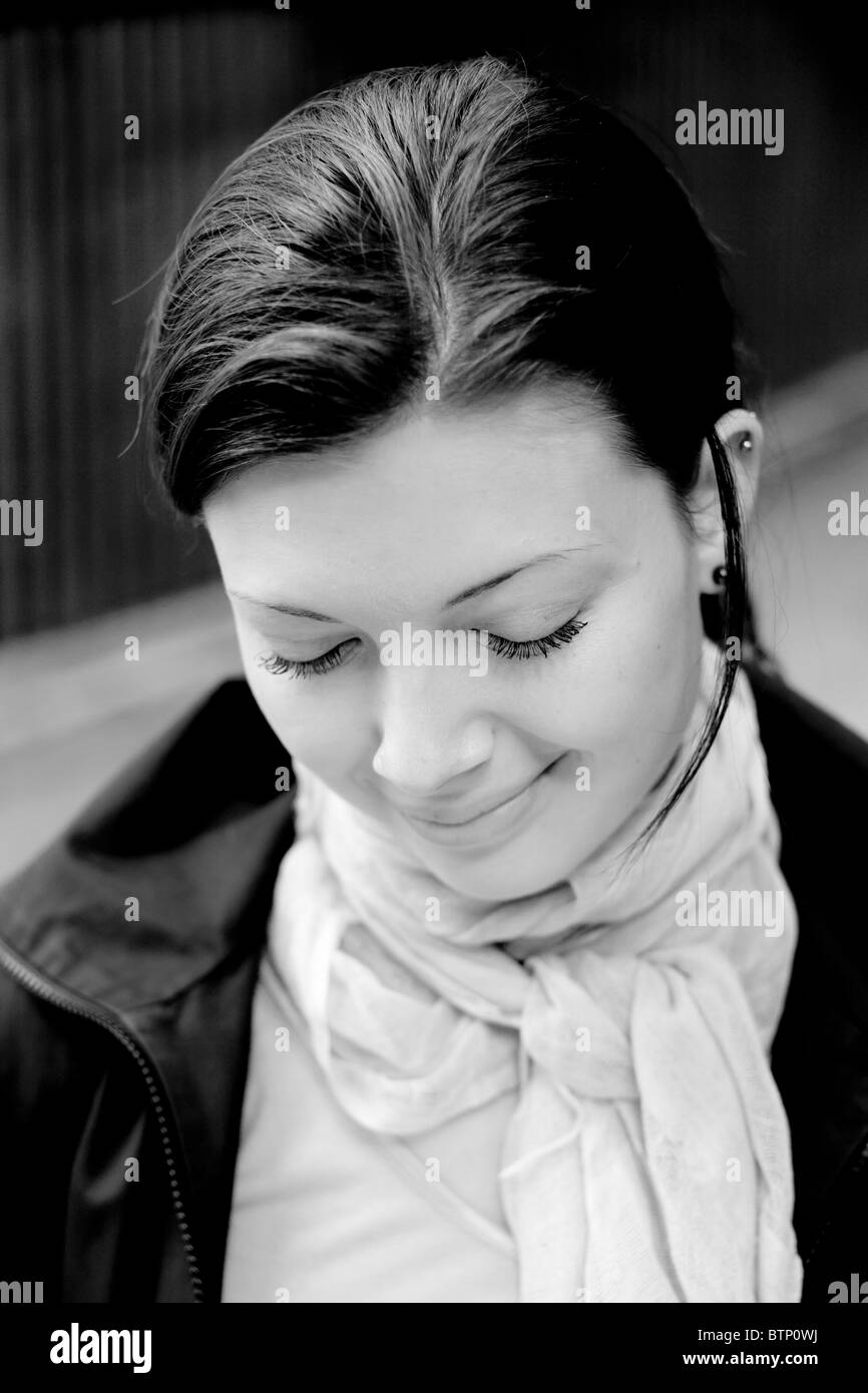 Schwarz-weißes Porträt einer Frau mit geschlossenen Augen, die sanft lächelt, einen Schal und eine Jacke trägt. Stockfoto