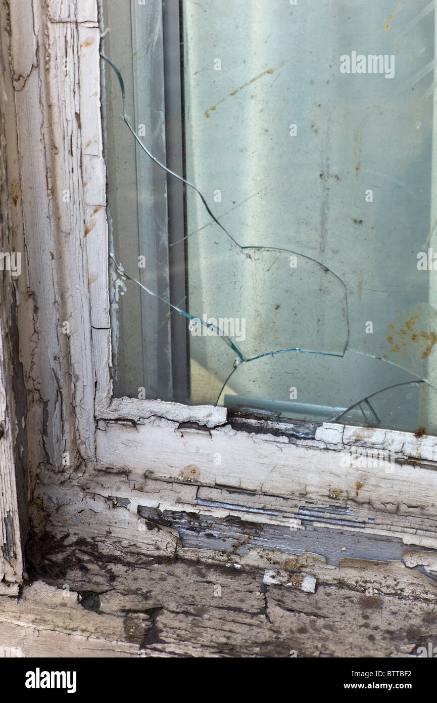 zerbrochene Fensterscheiben und abblätternde Farbe auf verfallenes Haus Stockfoto
