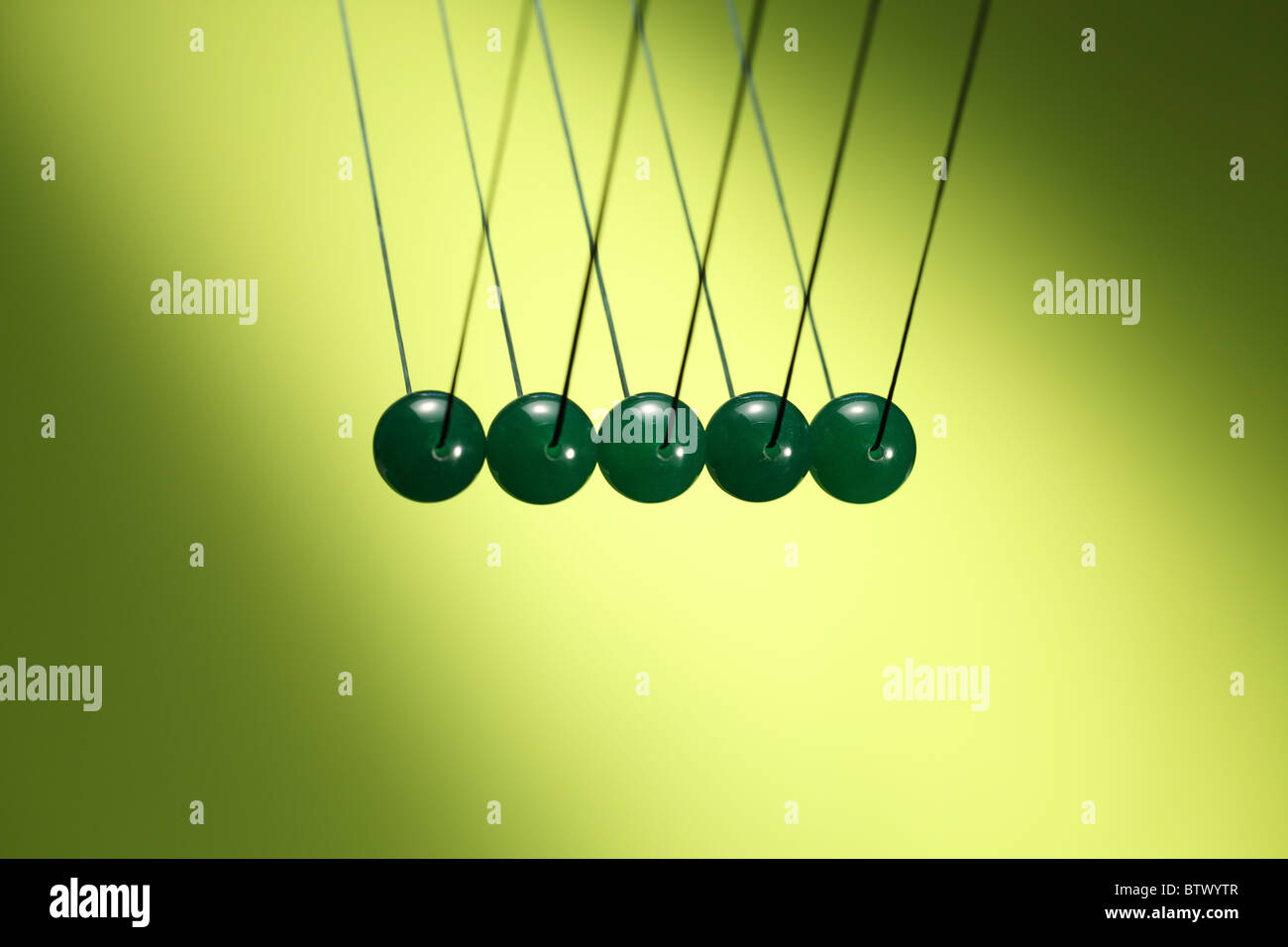Fünf grüne Murmeln in Reihe von Schnur hängen. Zeigt Newtons Wiege, ein Gerät, das der Impulserhaltung demonstriert. Stockfoto