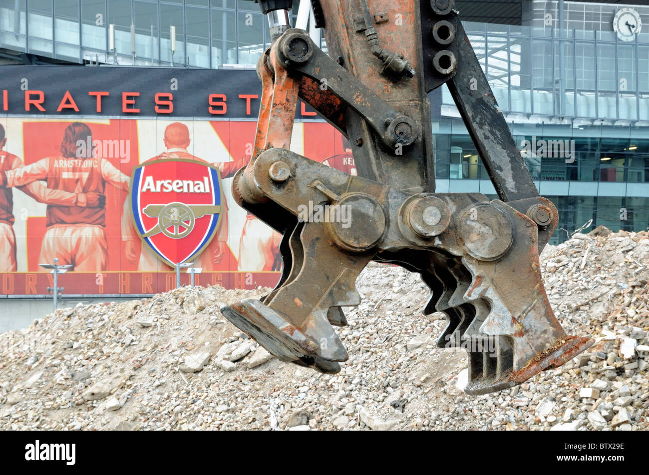 Abbruchstelle mit Pulverisator, Abbruchwerkzeug mit Arsenal Schild auf dem Emirates Stadium im Hintergrund Holloway London England UK Stockfoto