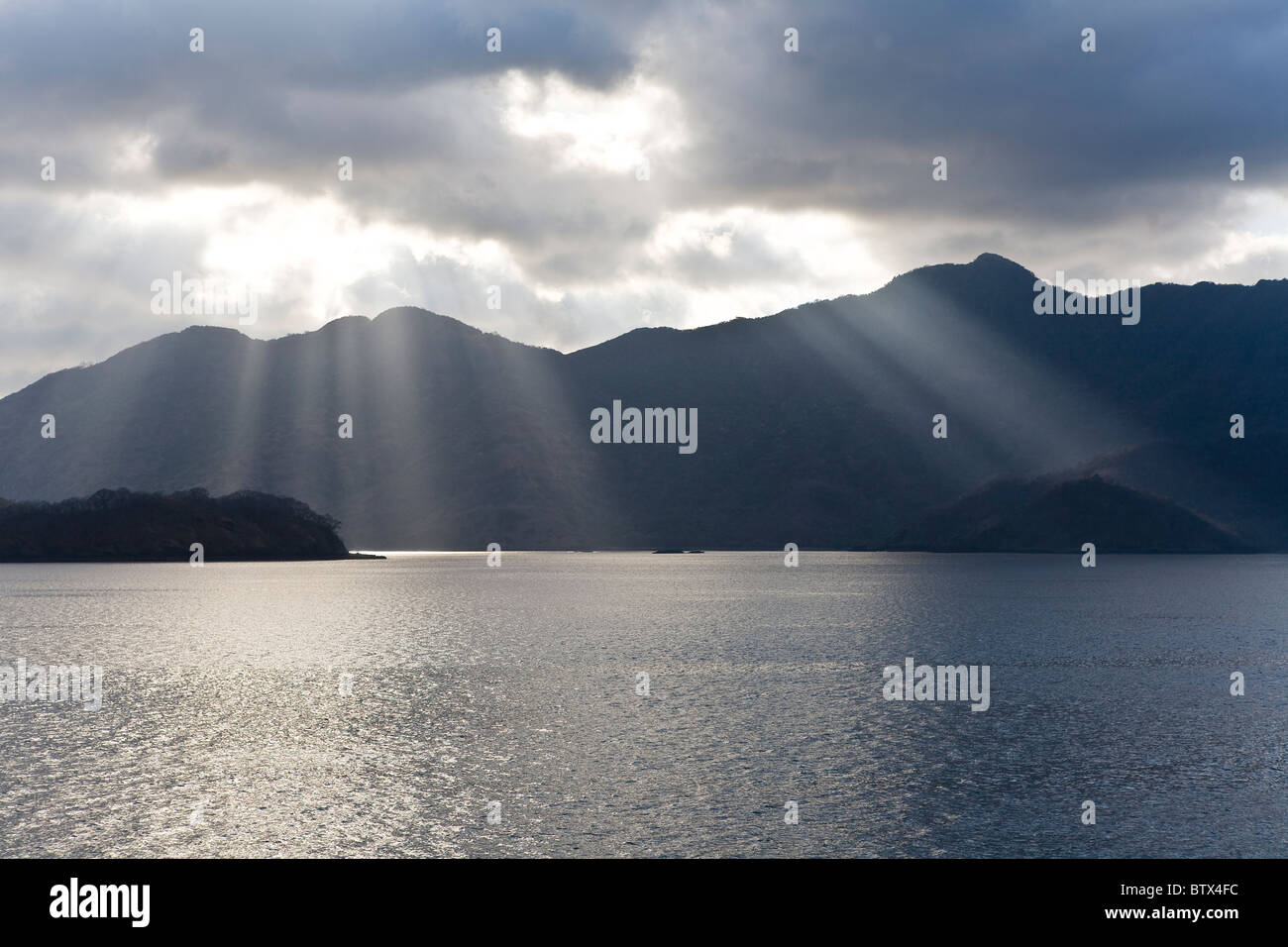 Am späten Nachmittag Kaskaden Sonnenlicht durch Wolkenabdeckung, die Beleuchtung des Wassers im Horseshoe Bay an der Südspitze der Insel Rinca. Stockfoto