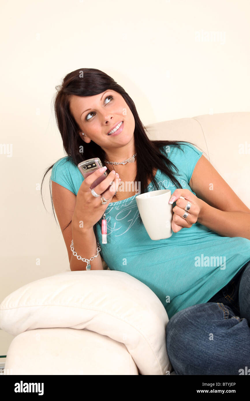 Junge Frau hält einen Becher und eine Handy-Sitzung blickte lächelnd Stockfoto