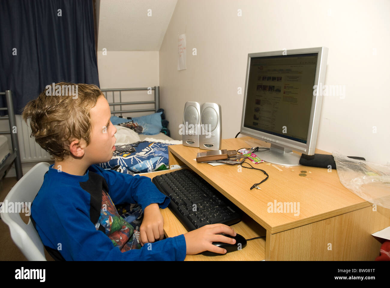 Ein kleiner Junge auf seinem Computer in eine unordentliche Schlafzimmer Stockfoto