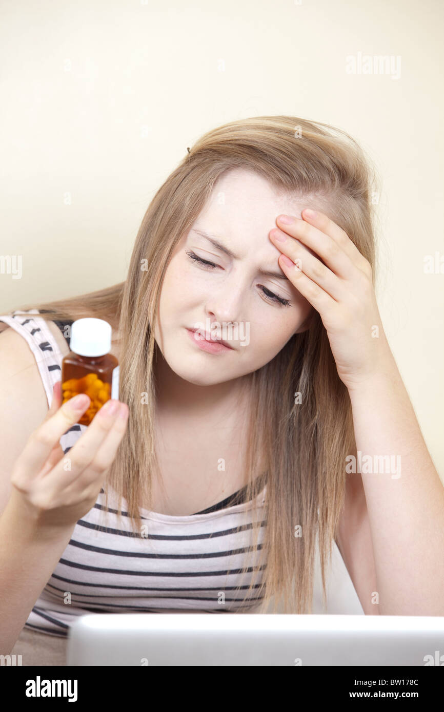 Ein junges Mädchen mit Kopfschmerzen prüft Hinweise auf eine Flasche Tabletten in ihr Schlafzimmer-UK Stockfoto