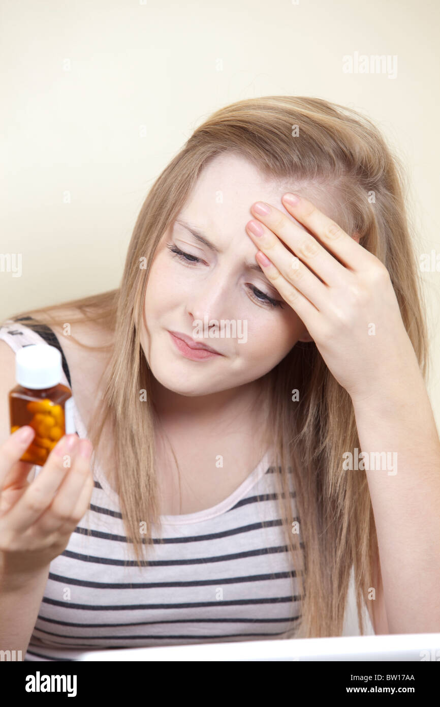 Ein junges Mädchen mit Kopfschmerzen prüft Hinweise auf eine Flasche Tabletten in ihr Schlafzimmer-UK Stockfoto