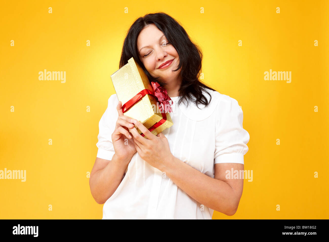Porträt des mittleren Alters weiblich mit goldenen Geschenkbox auf gelbem Hintergrund Stockfoto