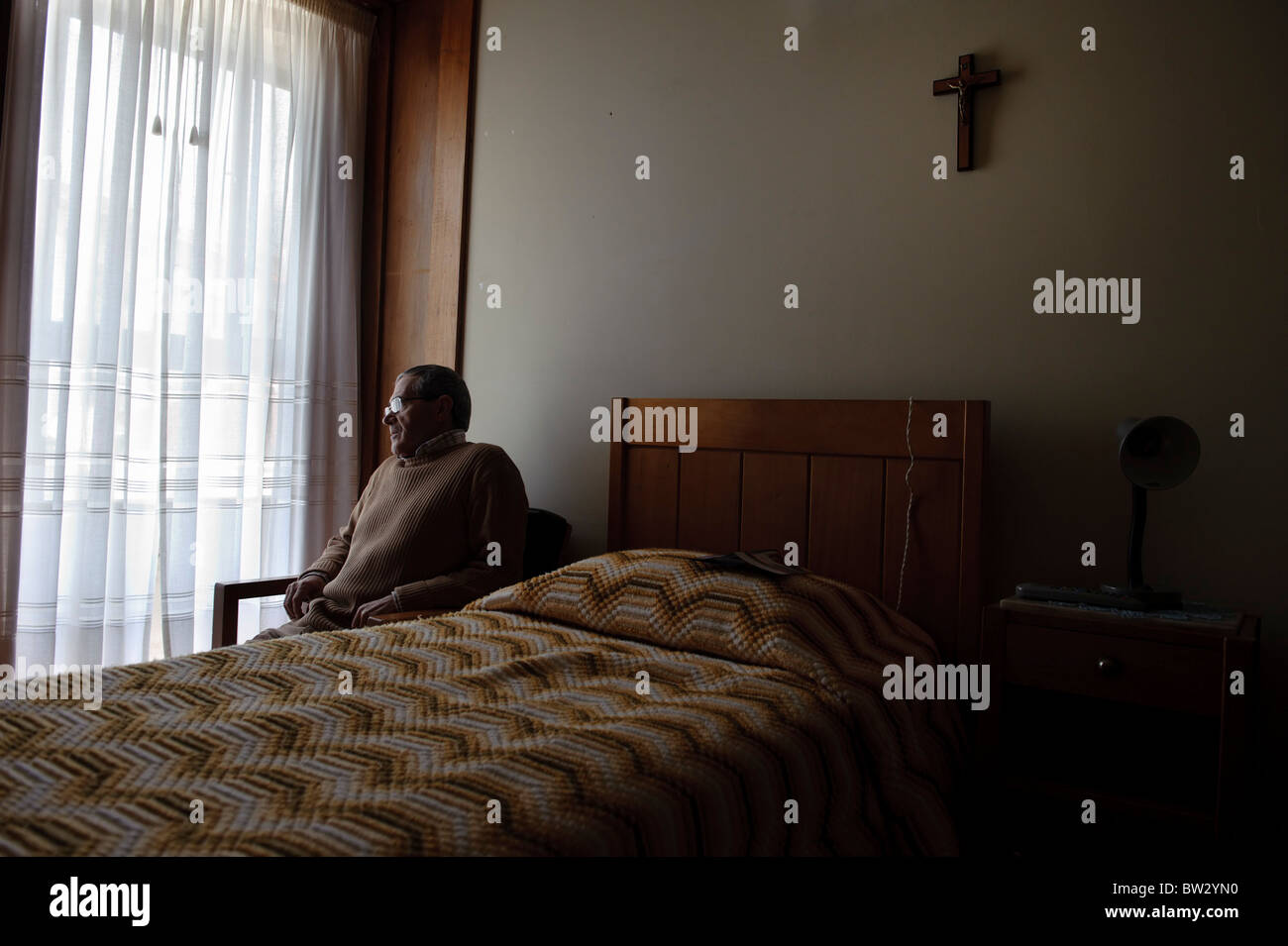 Senioren, die am Fenster allein in seinem Zimmer sitzen Stockfoto