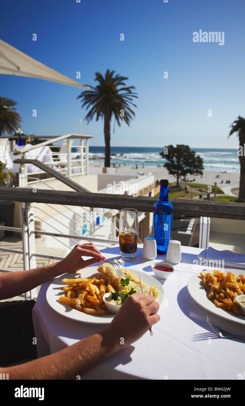 Frau Essen Fish &amp; Chips in Restaurant, Camps Bay, Cape Town, Western Cape, Südafrika Stockfoto