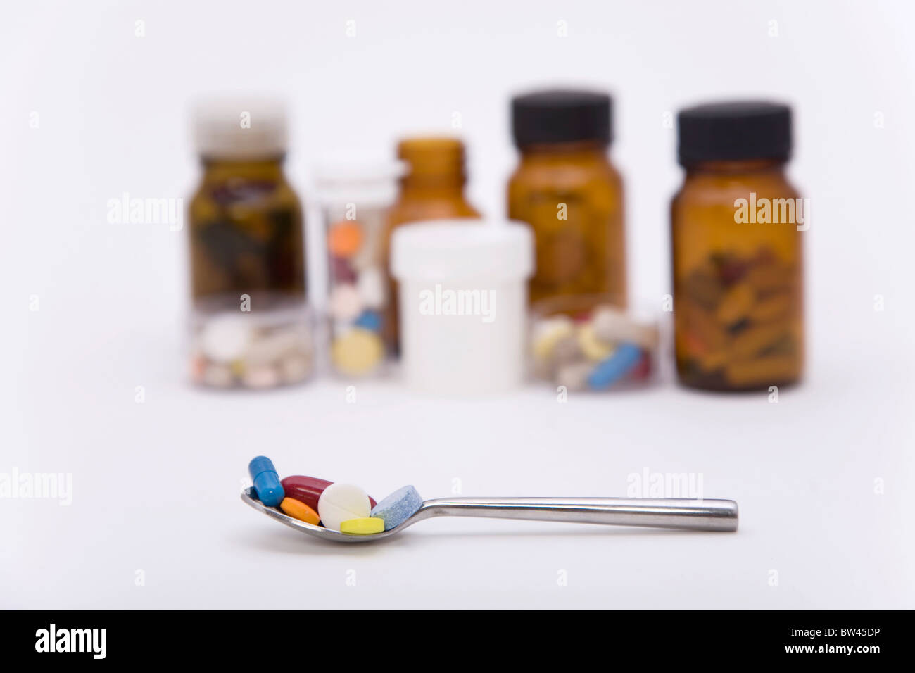 verschieden farbige Pillen in Löffel mit anderen Pillen auf dem Hintergrund Stockfoto