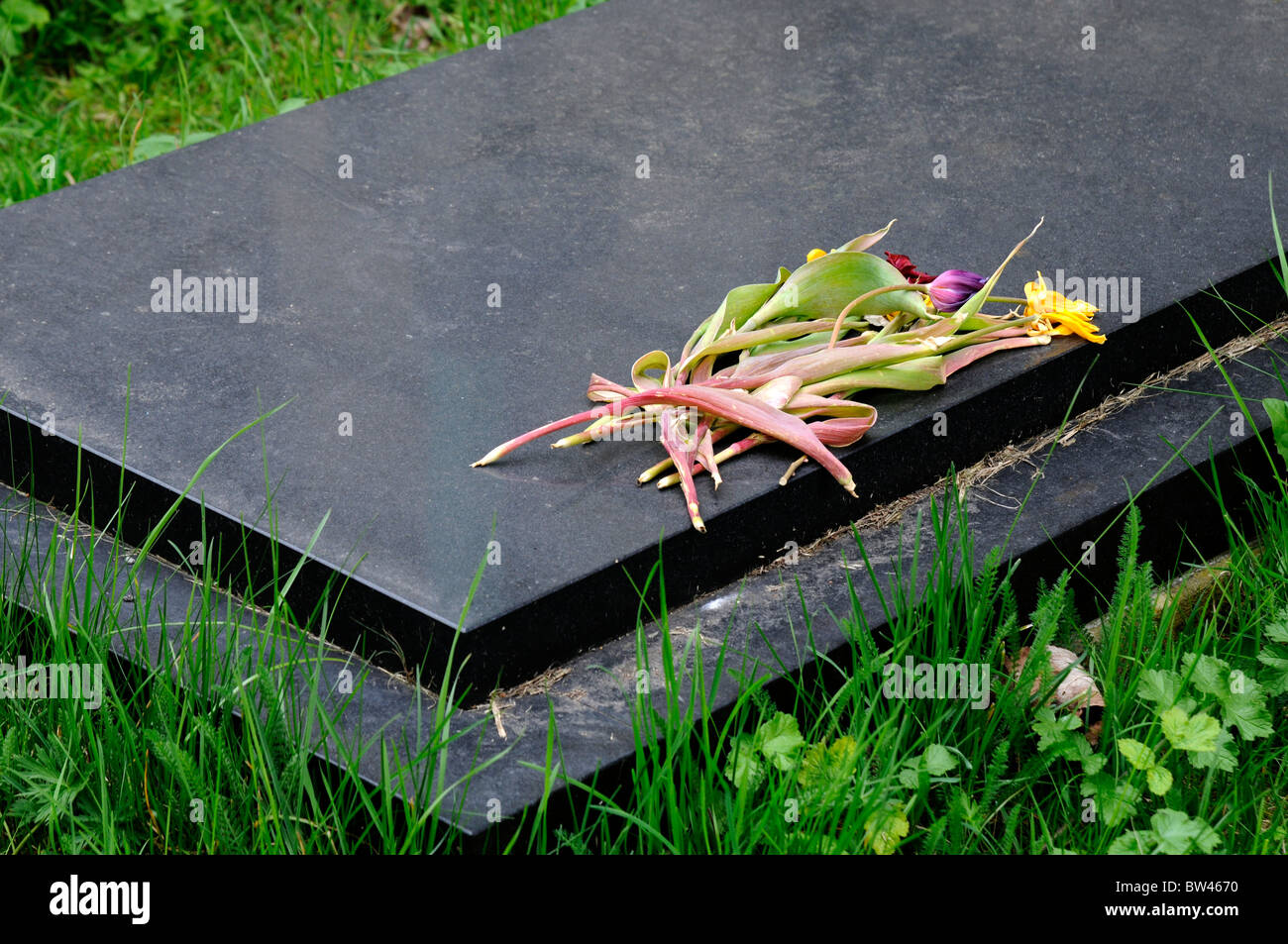 Ein Blumenstrauß verwelkt und tot auf dunklen Stein Grabstein Stockfoto