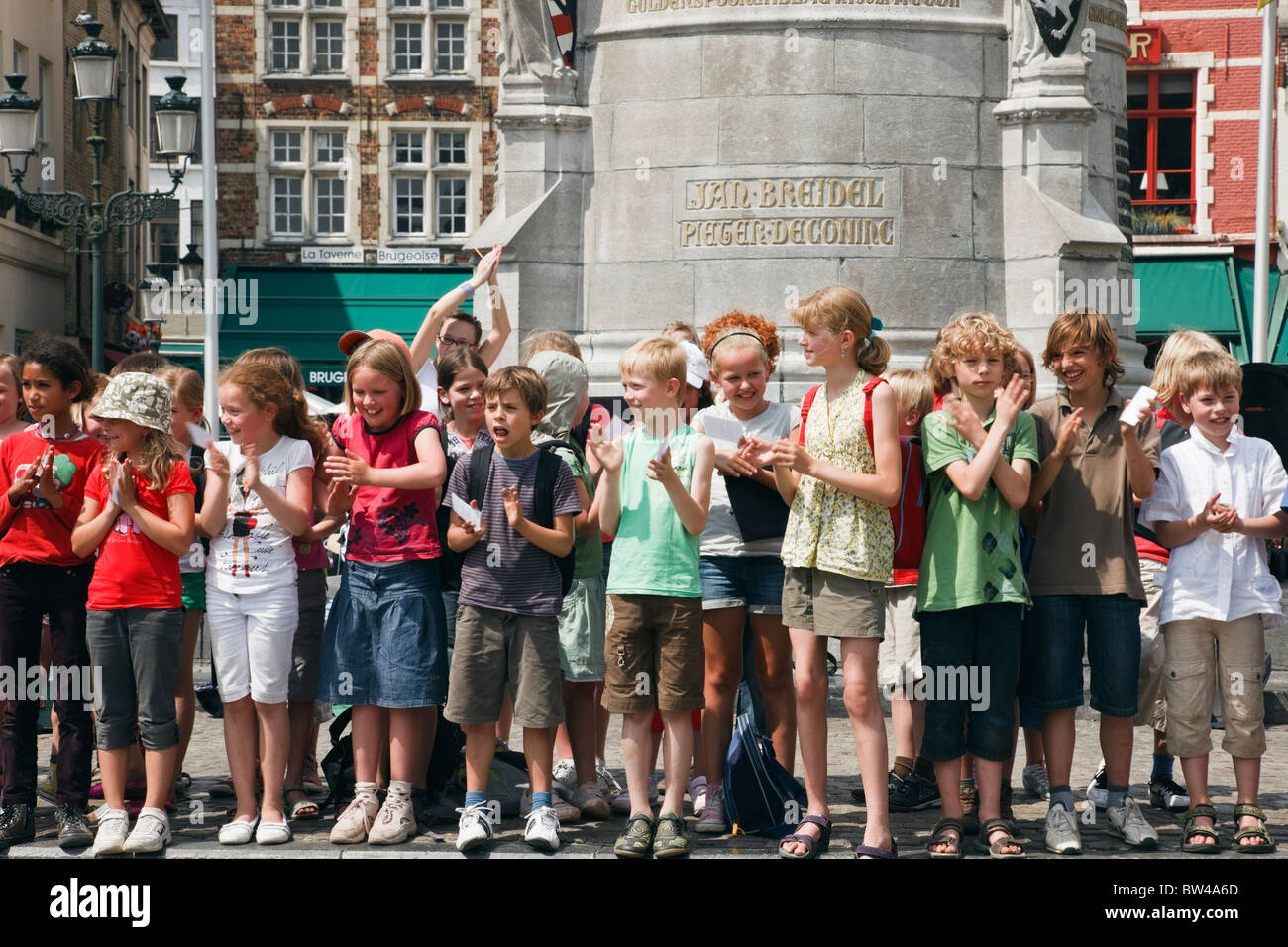 Markt, Brügge, Belgien. Gruppe von Kindern singen auf dem Altstadt-Platz mit dem Denkmal für die Helden des Brügge Matins Stockfoto