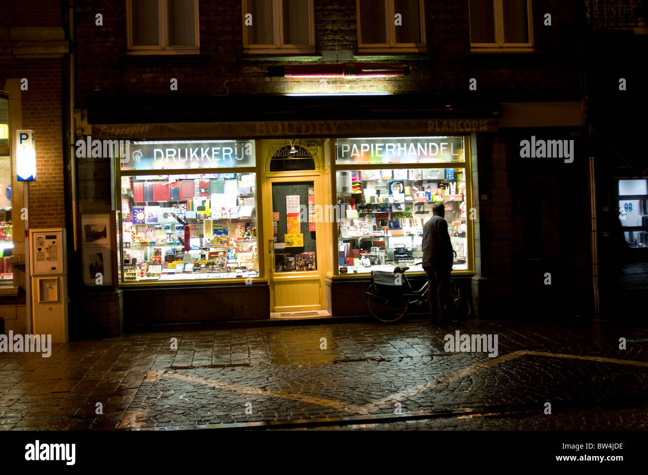 Ein Mann schaut in das Fenster eines Ladens einer nassen und windigen Nacht Ypern, Belgien Stockfoto