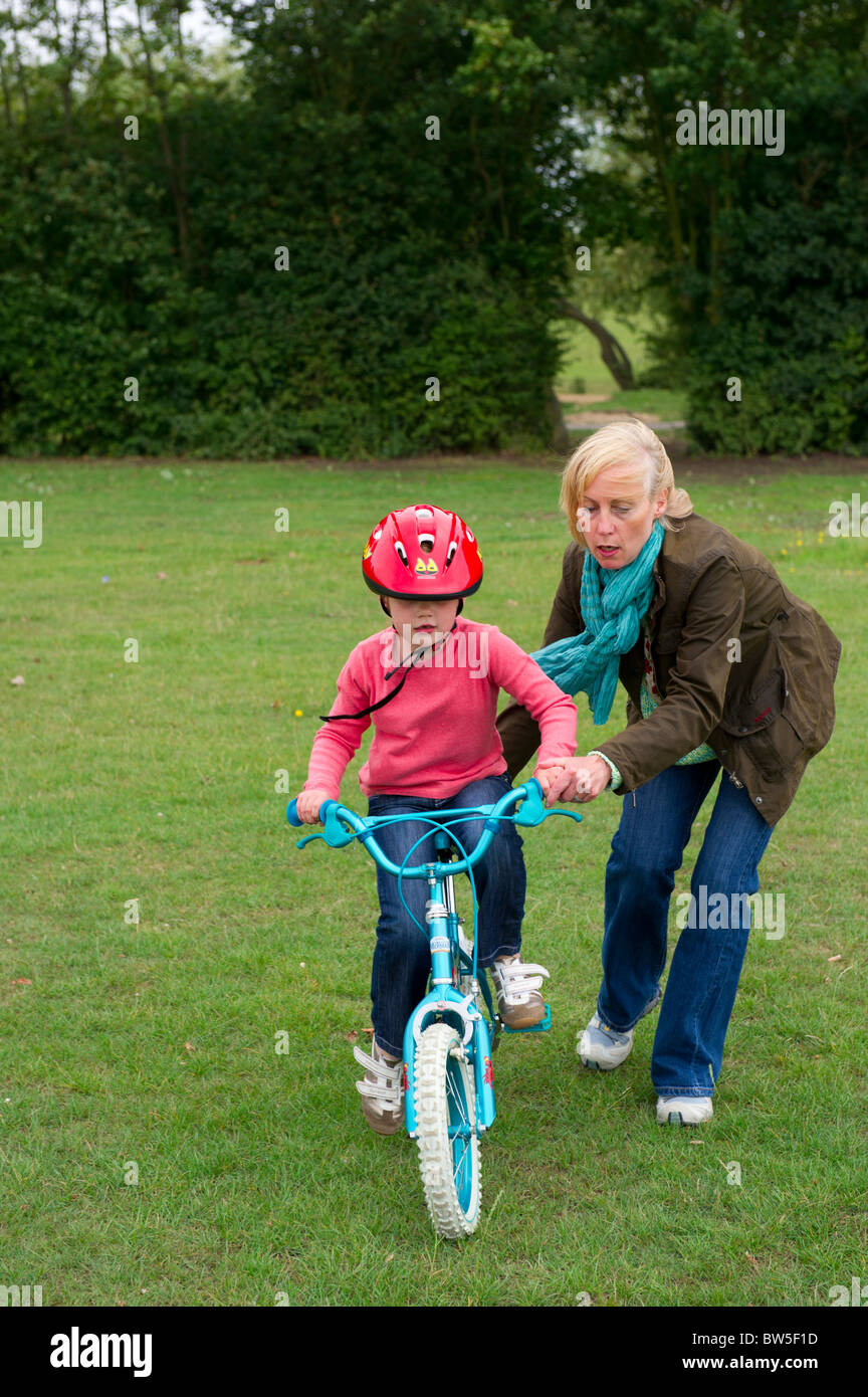 Mutter hilft jungen Tochter, mit dem Fahrrad ohne Stabilisatoren. Stockfoto