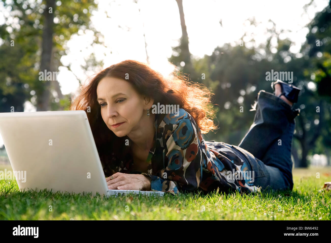 Porträt einer mittleren Alters Frau, ein Hörgerät zu tragen auf ihrem Laptop in einem Park. Stockfoto