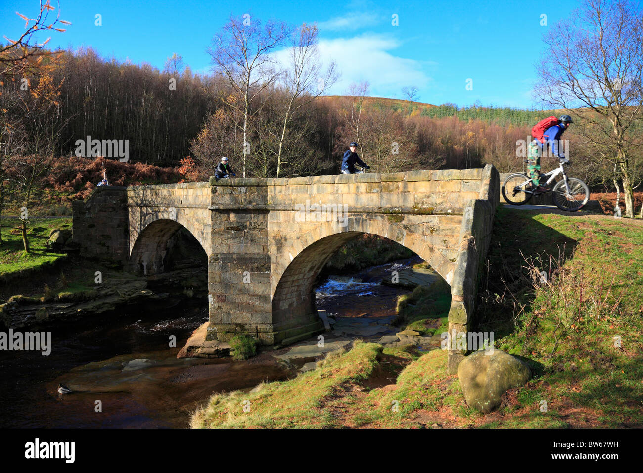 Radfahrer auf rutschigen Steinen Lastesel Brücke über den Fluss Derwent, Upper Derwent Valley, Peak District National Park, Derbyshire, England, UK. Stockfoto