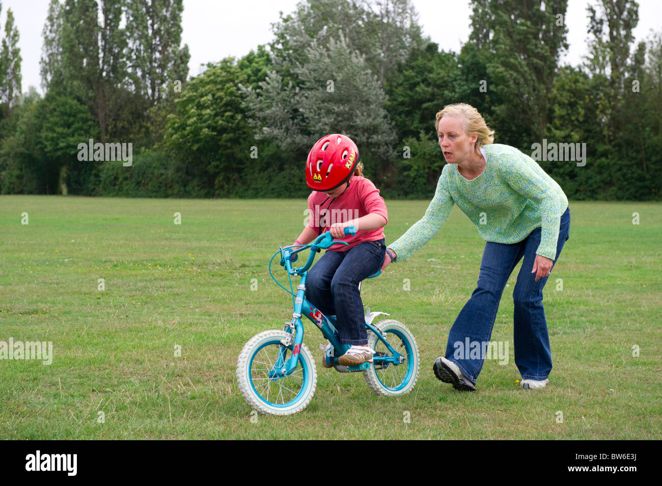 Mutter hilft jungen Tochter, mit dem Fahrrad ohne Stabilisatoren. Stockfoto