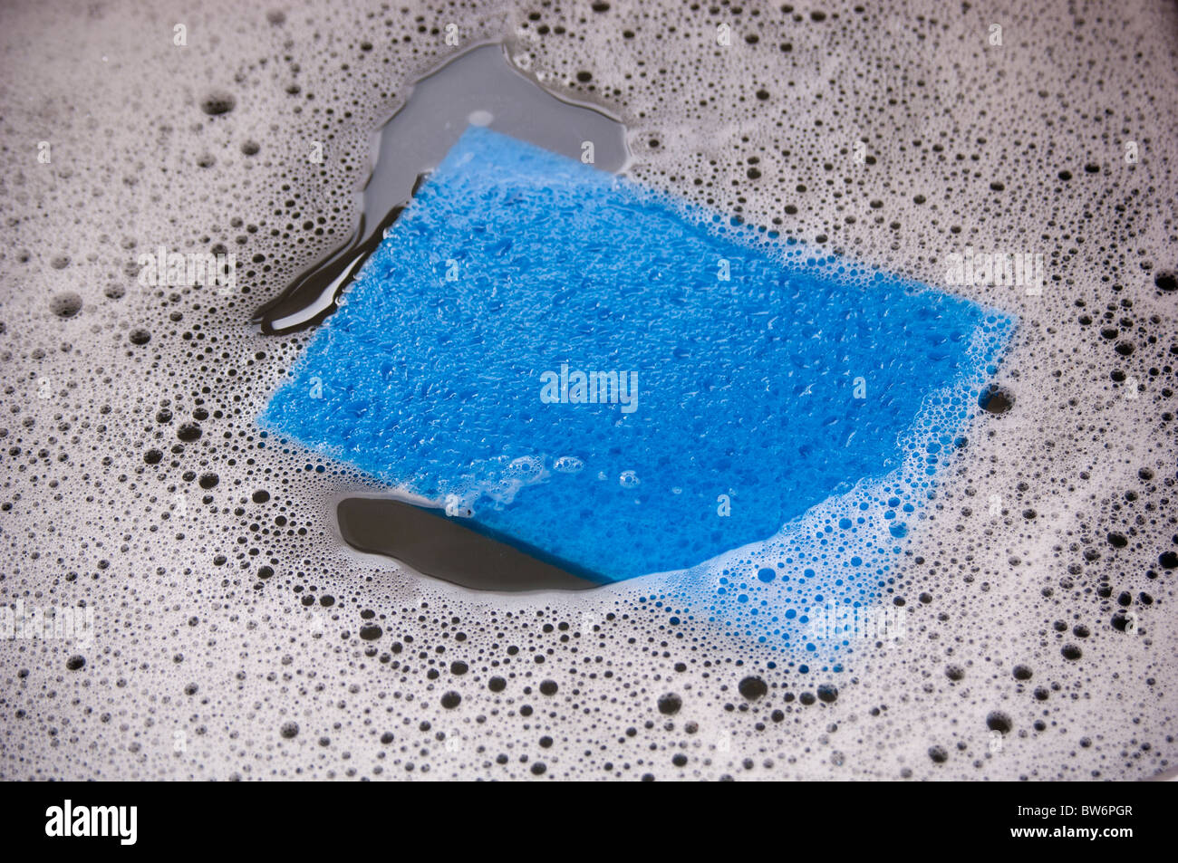 Blauer Schwamm und schmutzige Schale Wasser in ein Waschbecken Stockfoto