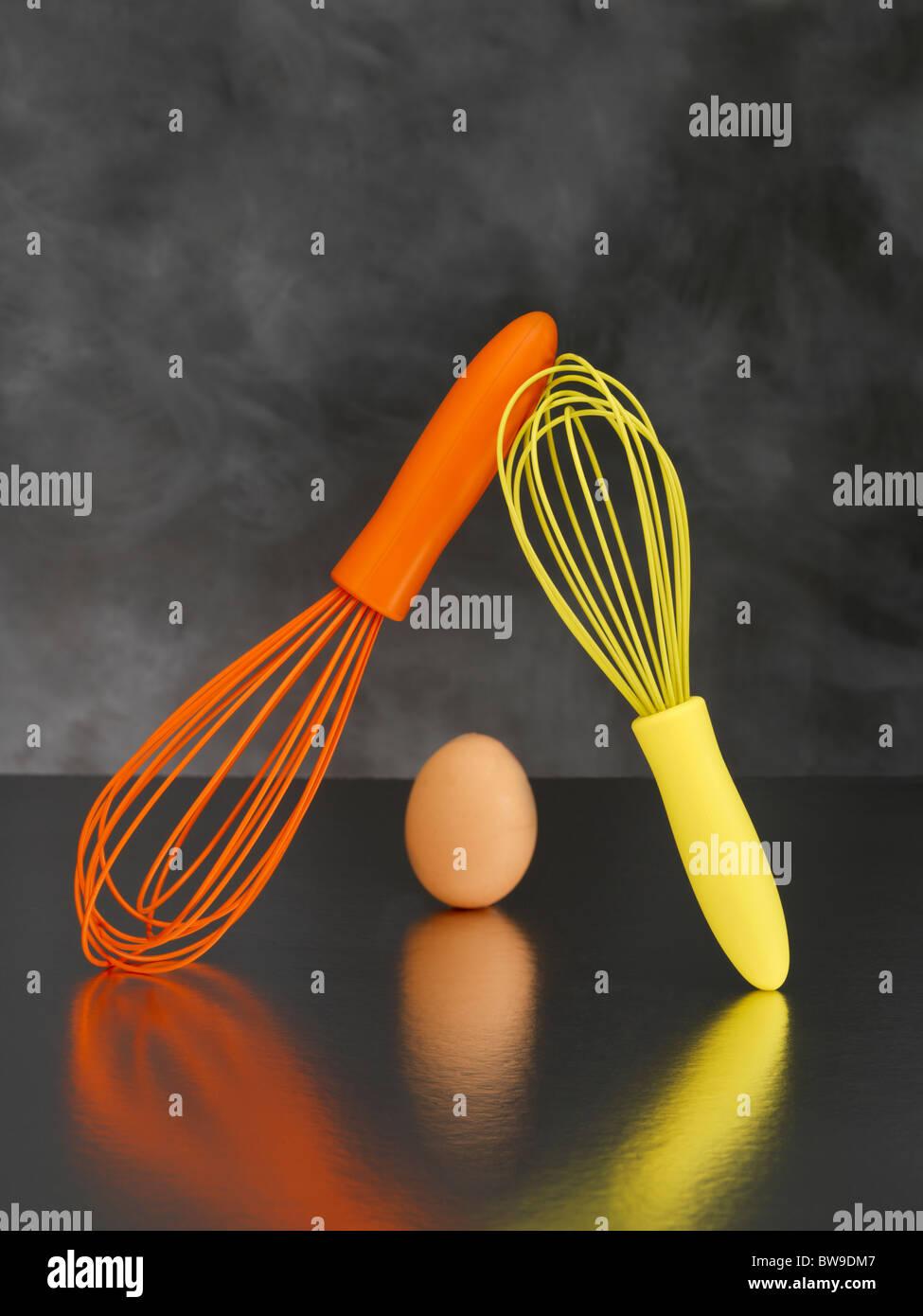 Eine Orange und eine gelbe Schneebesen und ein Ei auf einem grauen Hintergrund Stockfoto