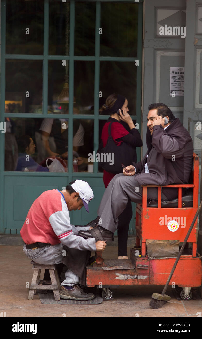 Schuhe Schuh Glanz Polieren mans, während er am Handy spricht, ist eine Frau auf einem Handy im Hintergrund, Cuenca, Ecuador Stockfoto