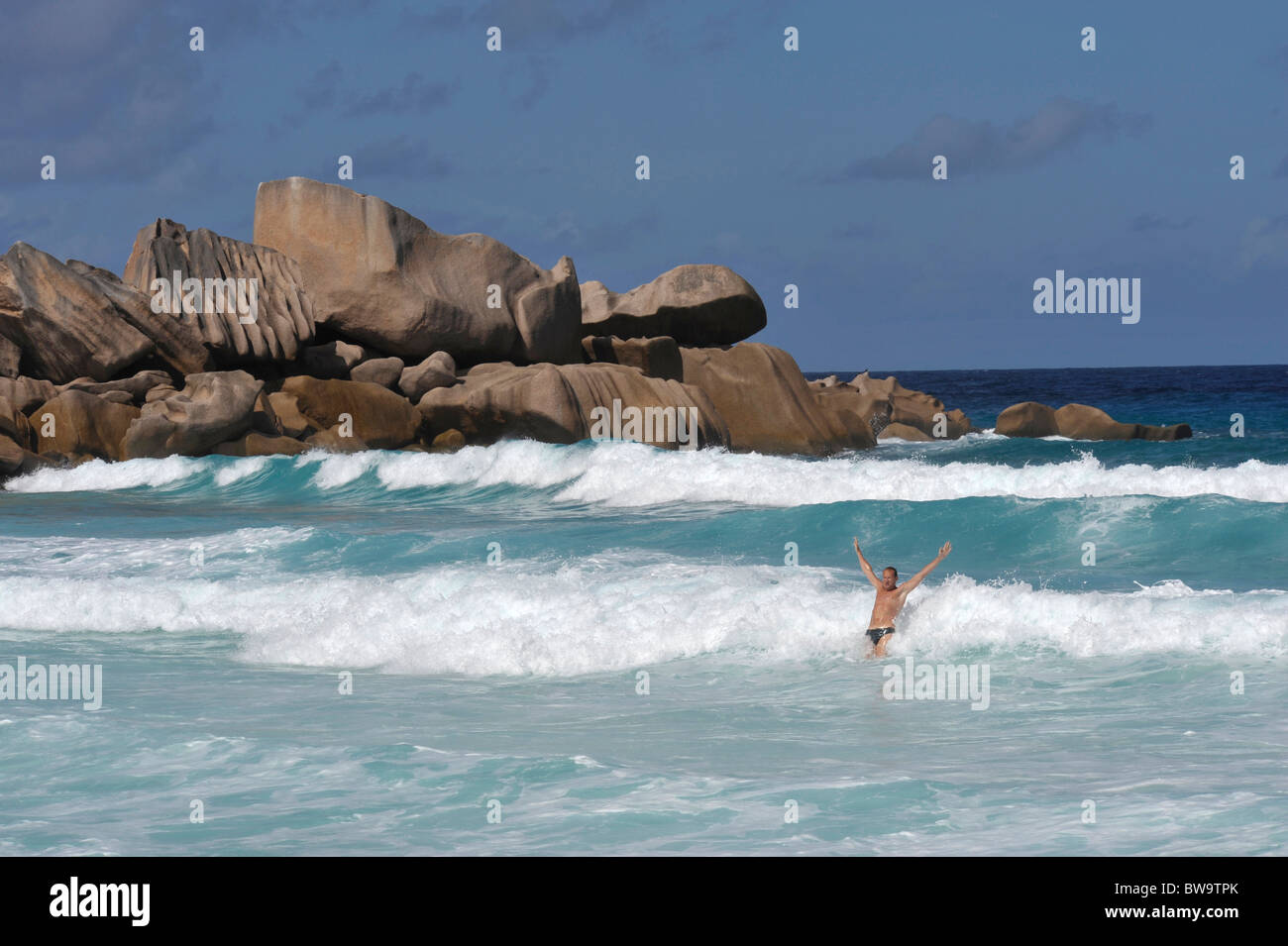 Mann mit Arme nach oben in die Luft stehen in Wellen am Grand Anse, La Digue, Seychellen Stockfoto