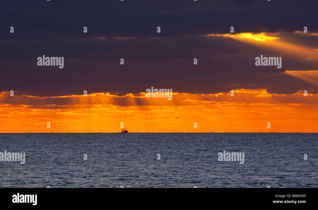Fischerei Trawler Schiff Richtung Heimat aus dem Meer bei Sonnenuntergang, wie roll-dunkle Wolken in Brighton, England Stockfoto