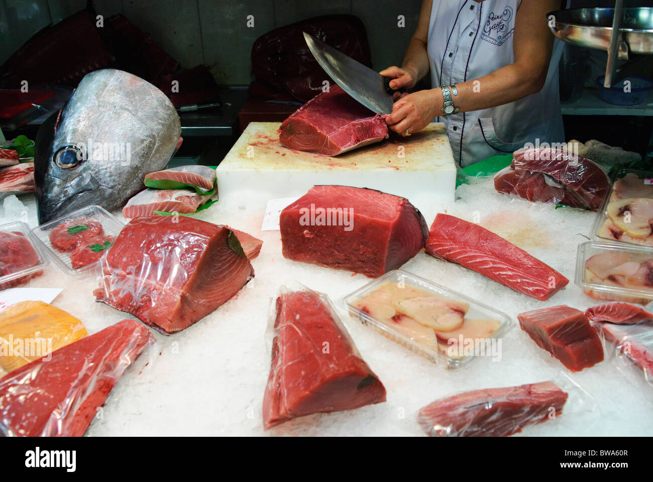 Frau schneidet ein Stück frischen Thunfisch mit großen Messer am Stall in La Boqueria-Markthalle in Barcelona, Spanien Stockfoto