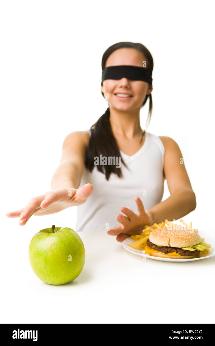 Porträt des jungen Mädchens in Augenbinde dehnen ihre Hand in Richtung grüner Apfel und Einlagern von Fast-food Stockfoto