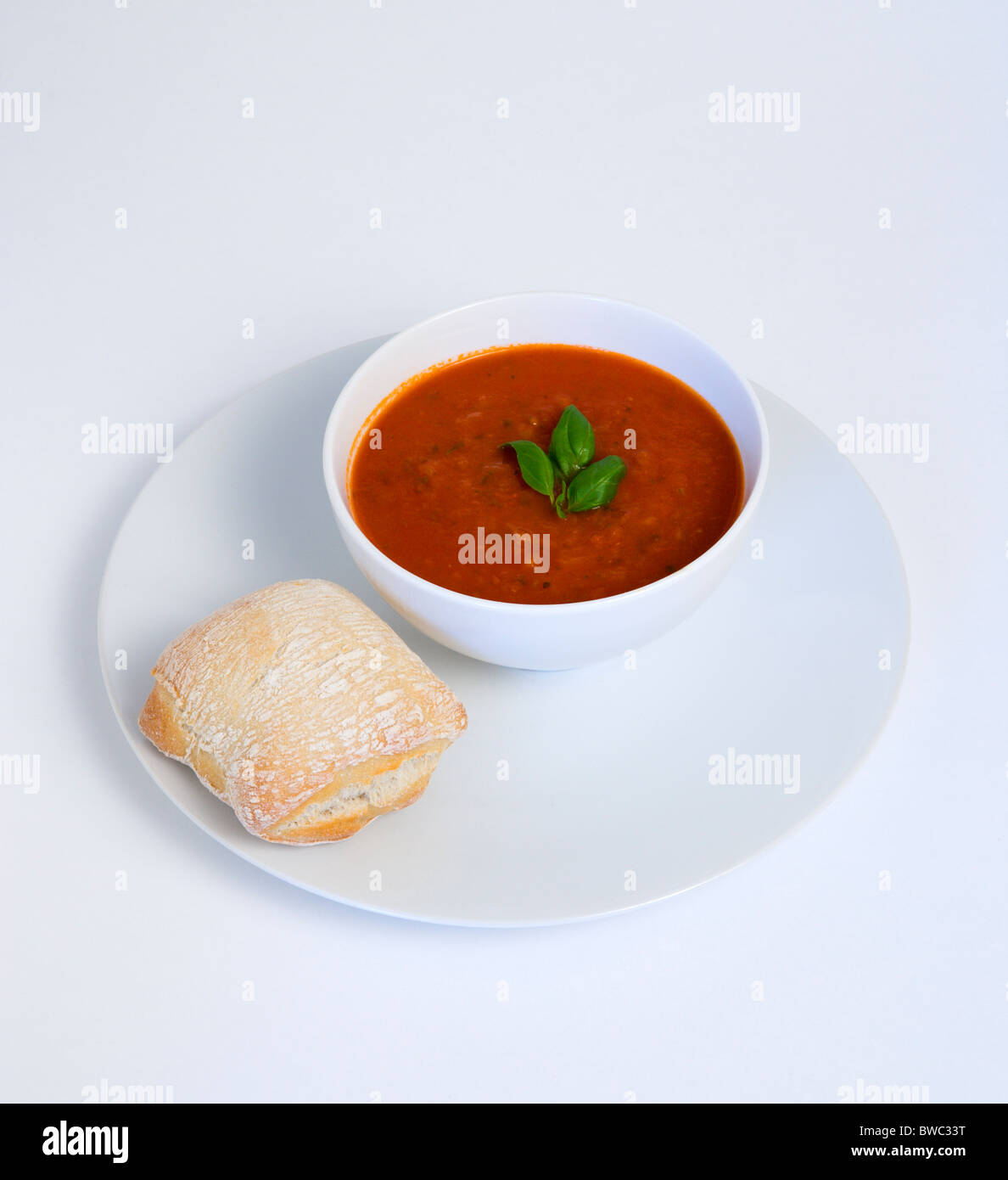 Essen, gekochte, Suppe, Schüssel mit Tomaten und Basilikum Suppe auf einem Teller mit einem rustikalen Brot Rollen auf einem weißen Hintergrund. Stockfoto