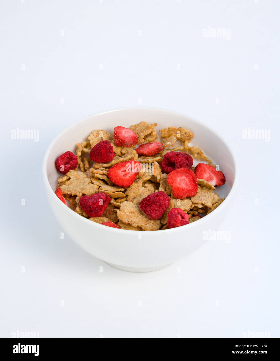 Essen, Speisen, Müsli, weiße Frühstück Schüssel mit Kleie-Flocken-Müsli mit Einfrieren getrocknete Früchte der Erdbeeren und Himbeeren in Milch Stockfoto