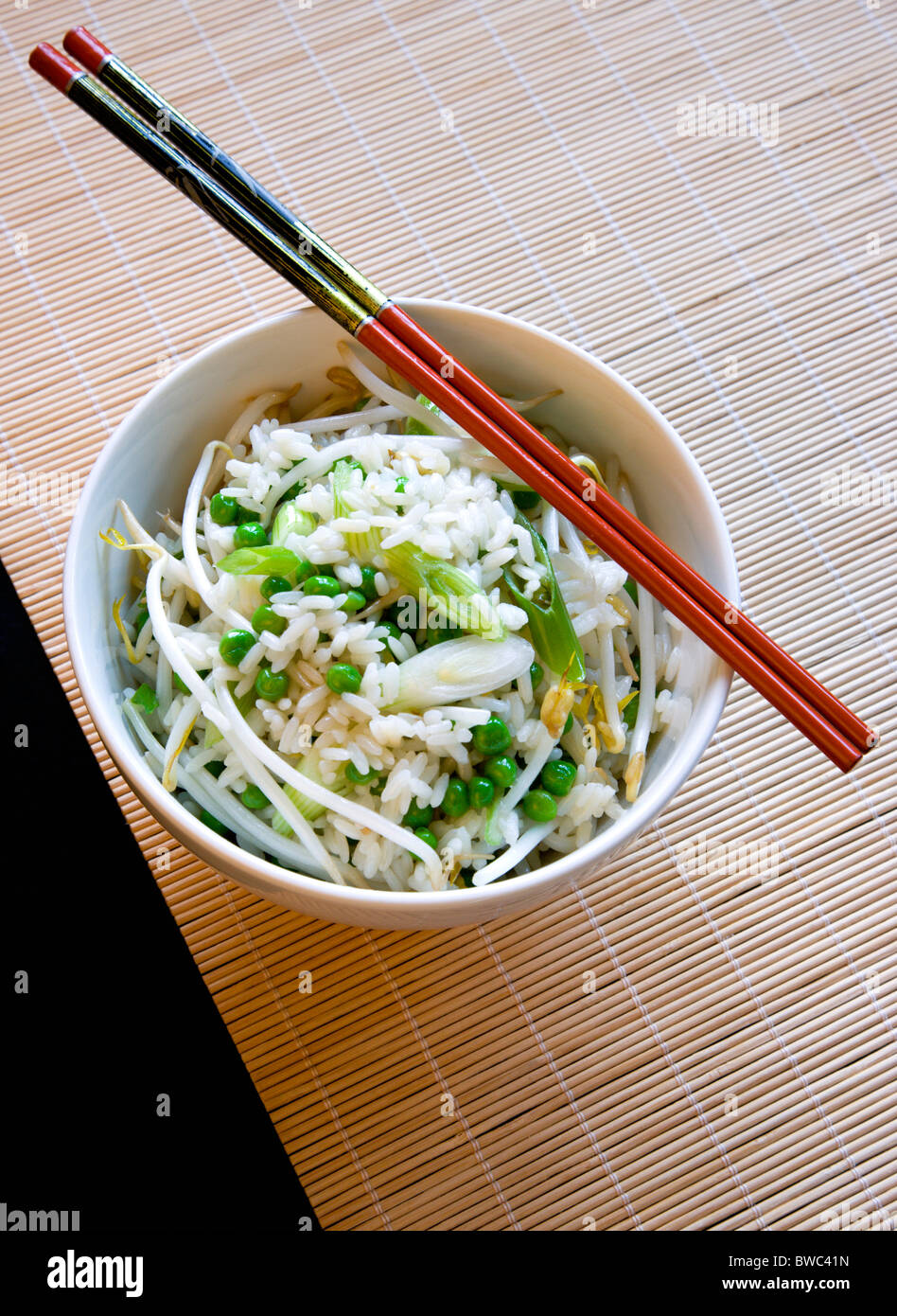 Essen, gekochte, Reis, gebratener Reis mit Gemüse in eine Schüssel geben mit Stäbchen auf einer Bambusmatte Tisch sitzen. Stockfoto