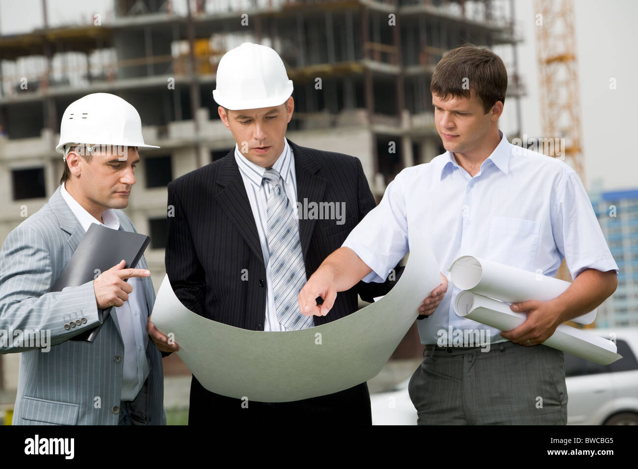 Porträt von drei Bauherren am Baustelle stehen und diskutieren neue Projekt von einer von ihnen gehaltenen Stockfoto
