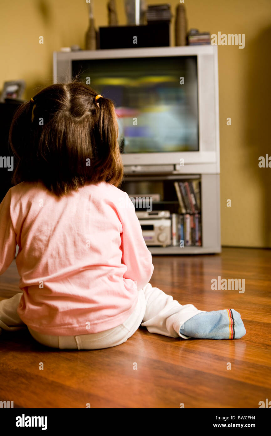 Heckansicht des kleines Mädchen auf dem Boden sitzend und Zeichentrickfilme im Fernsehen zu Hause Stockfoto