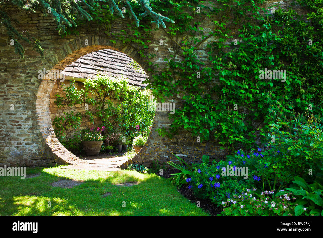 Eine kreisförmige Öffnung in eine Gartenmauer mit Blick über den Garten hinaus. Stockfoto