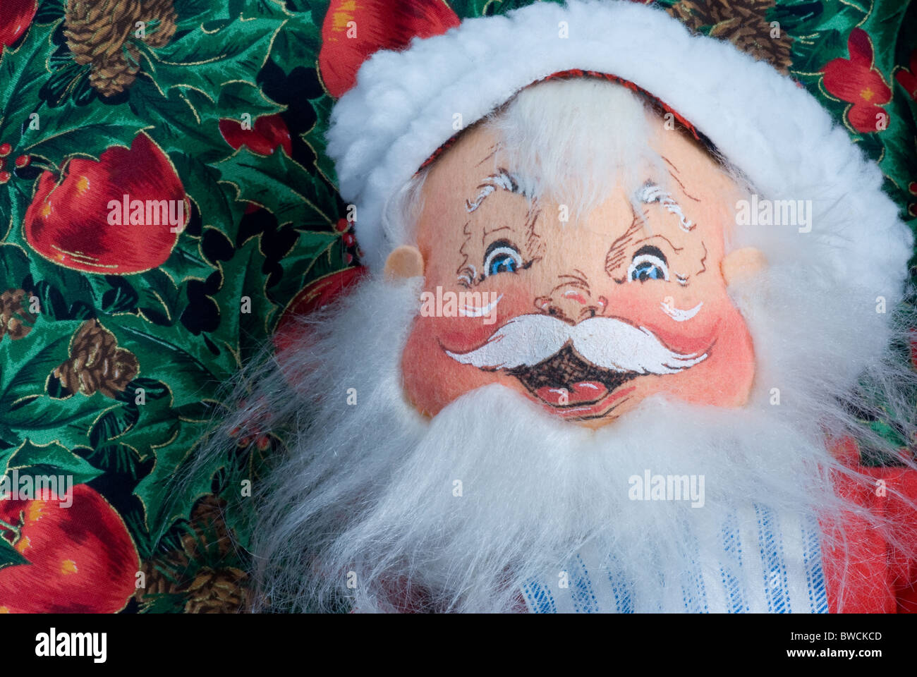 Lächelnder Weihnachtsmann aus der Nähe. Bemaltes Stoffgesicht mit Hut und Bart auf Apfel- und StechHintergrund. Stockfoto