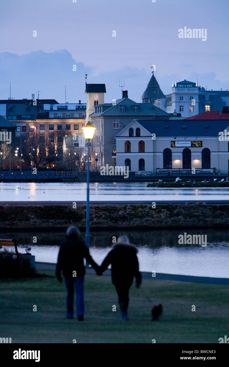 Menschen zu Fuß entlang Tjörnin-Sees. Die Innenstadt von Reykjavik, Island. Stockfoto