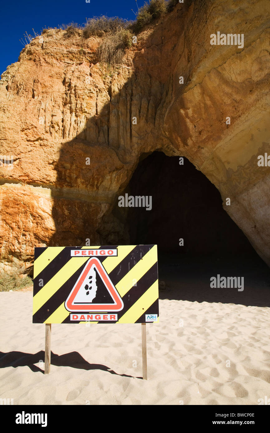Ein Schild Warnung vor Steinschlag vor einer Höhle am Strand von Praia da Rocha. Stockfoto