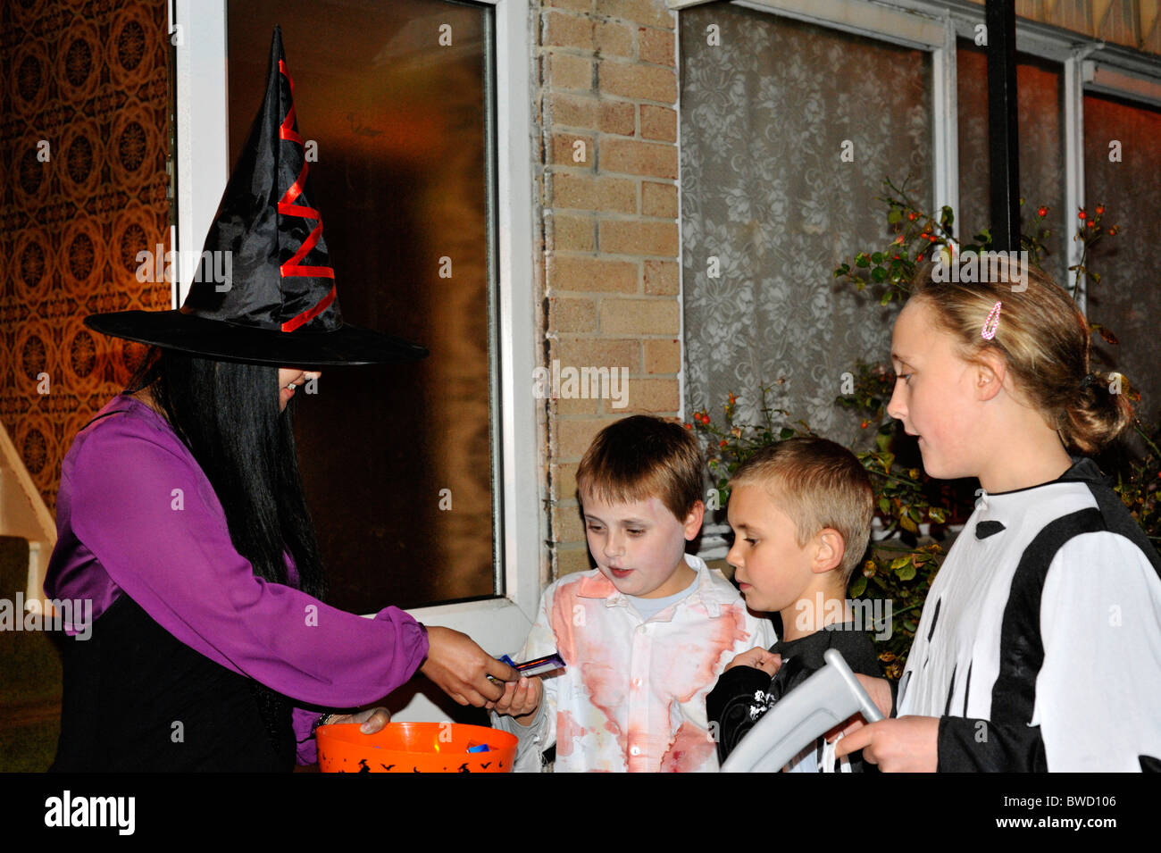 Frau verkleidet als Hexe den Kindern Süßigkeiten und Bonbons während Halloween Süßes oder Saures Stockfoto