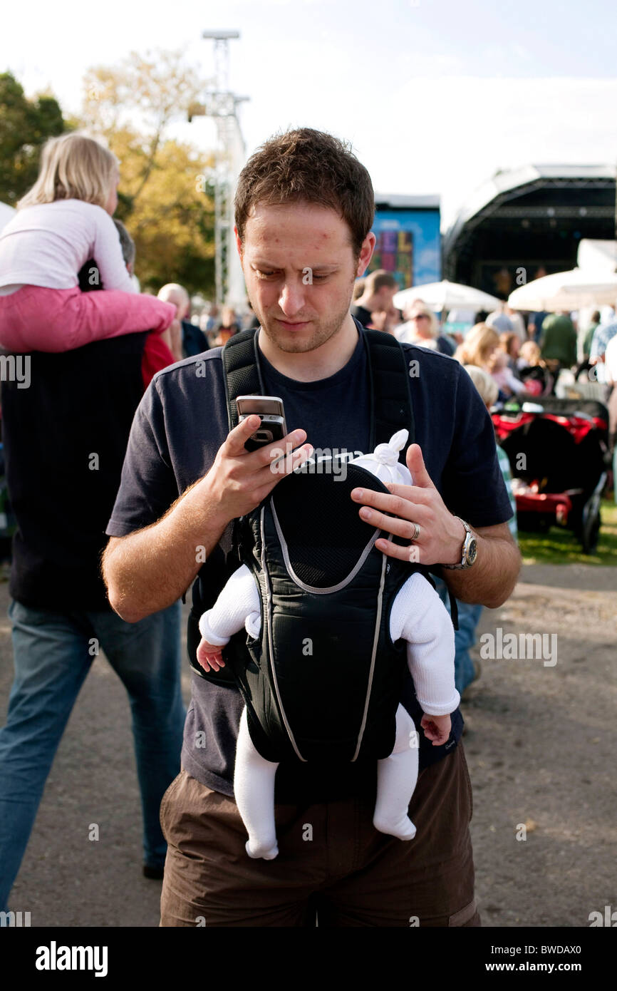 Ein Vater hält seine jungen Baby in einem Papoose mit einer Hand, während in der anderen er SMS auf seinem Handy ist. DAVID MANSELL Stockfoto