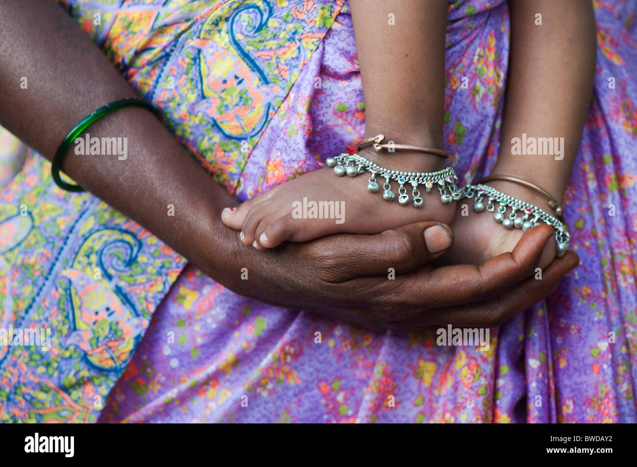 Indische Babys Füße auf Mütter Hände gegen bunte Kleidung. Andhra Pradesh, Indien Stockfoto
