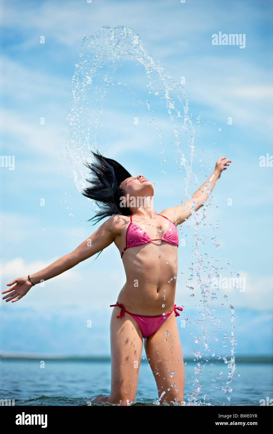 Frau spritzt sich Wasser am Strand Stockfoto