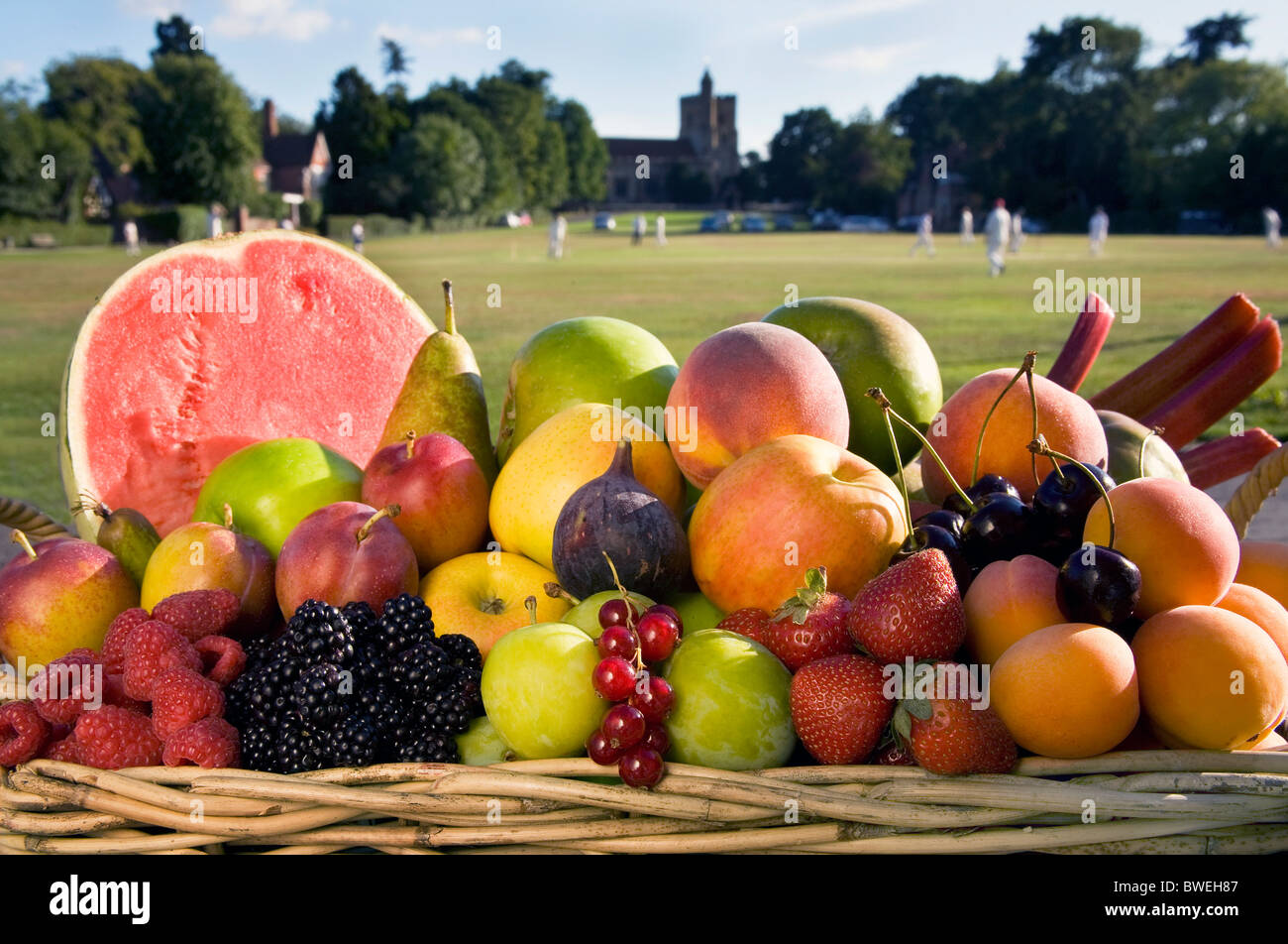 Korb mit köstlichen frischen gesunden britischen Sommerfrüchte im Korb neben Benenden Dorfanger mit Cricket-Match Kent UK Stockfoto