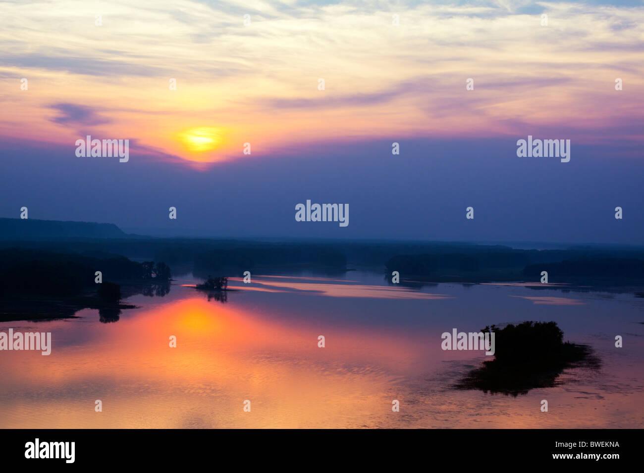 Die Sonne geht durch eine Schicht von Wolken über dem Wasser des Mississippi River in der Nähe von Savanne, IL. Stockfoto
