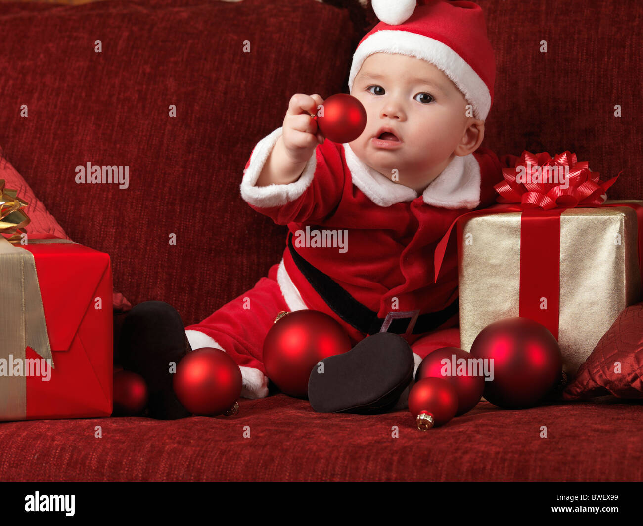 Lizenz erhältlich unter MaximImages.com - ein sechs Monate alter Junge trägt Weihnachtsmann-Kostüm und hält eine rote Kugel in der Hand Stockfoto