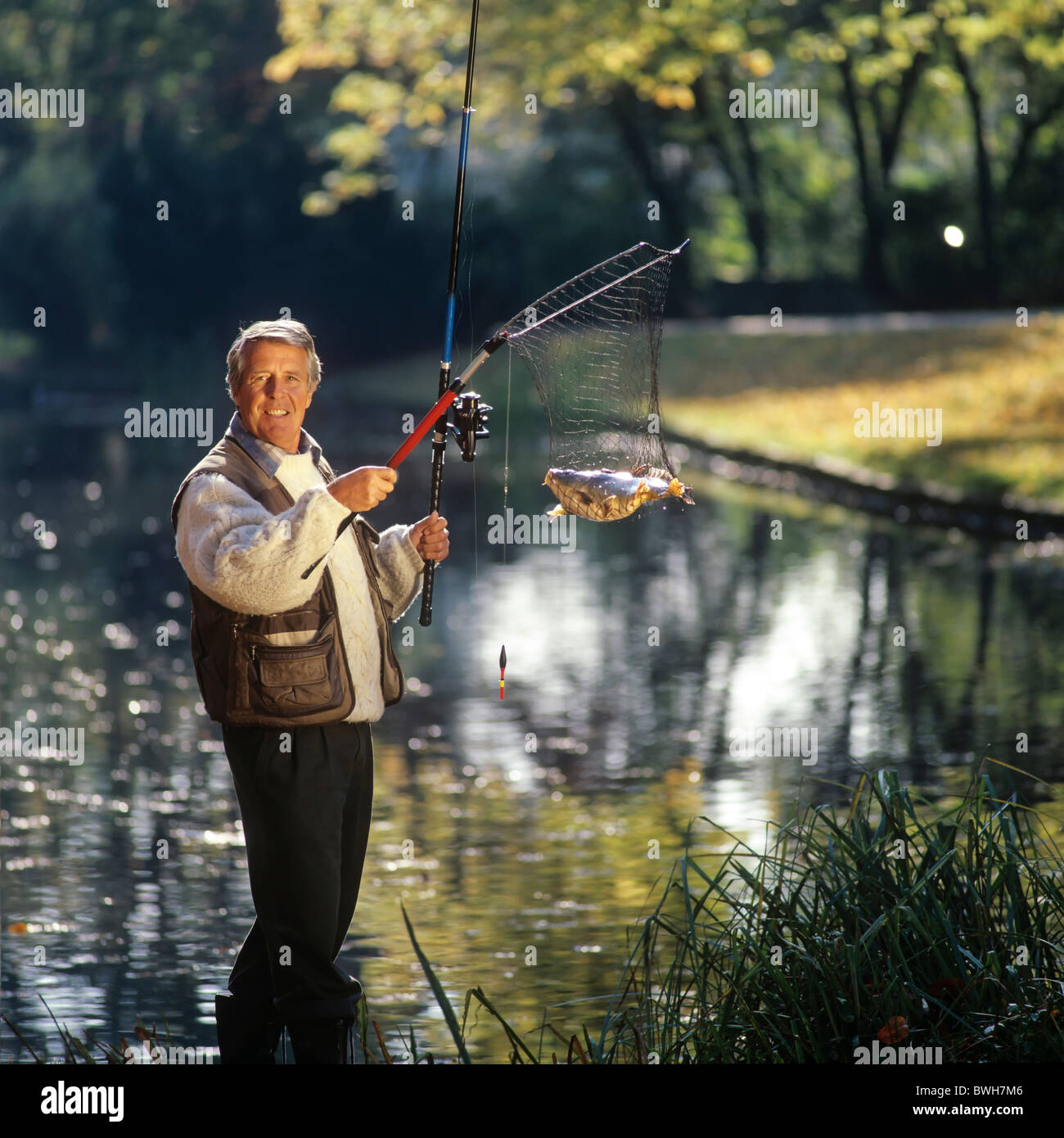 Senior Angler an einem Teich mit einem Fisch im Netz Stockfoto